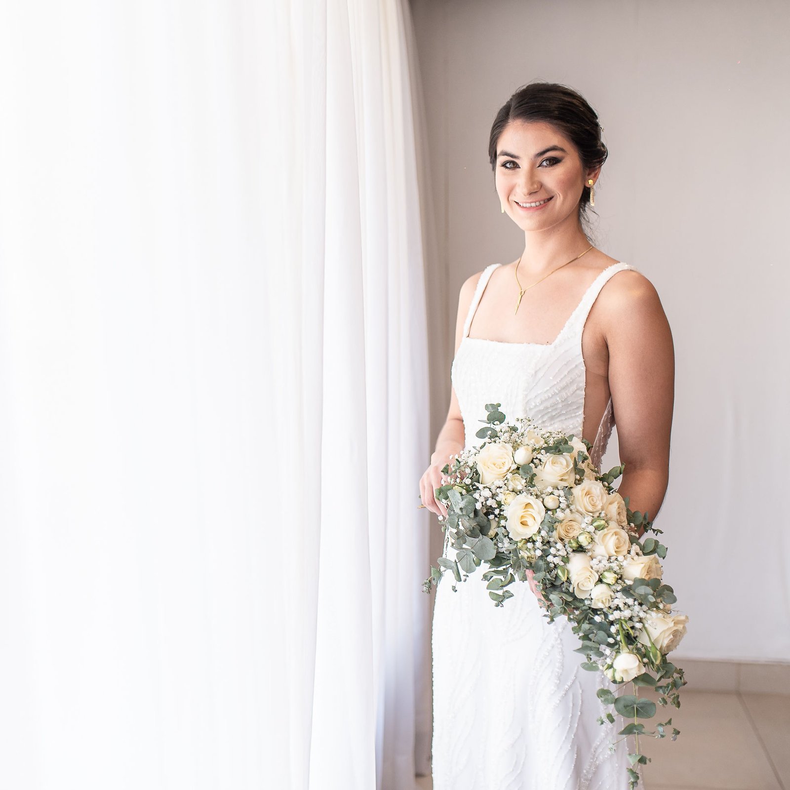Novia sonriente junto a una ventana, con su ramo de novia